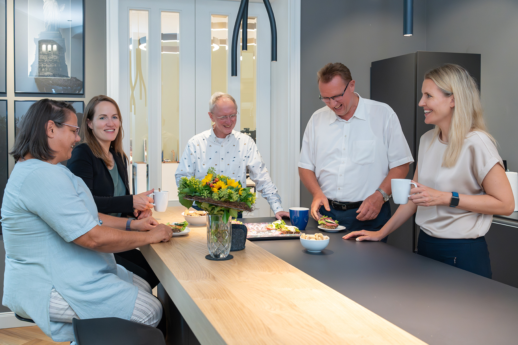 Mehrere Mitarbeitende der Rose Treuhand GmbH unterhalten sich in der modernen Kanzlei-Küche bei Kaffee und Snacks.