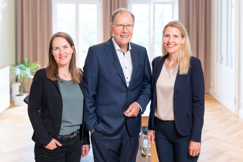 Drei Mitglieder des Teams der Rose Treuhand GmbH posieren gemeinsam im Büro am Olivaer Platz in Berlin.